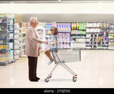 Foto completa del profilo di nonna con un bambino in un carrello della spesa in un supermercato Foto Stock