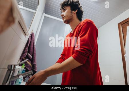 Giovane uomo che lava le mani nel lavandino del bagno con camicia rossa Foto Stock