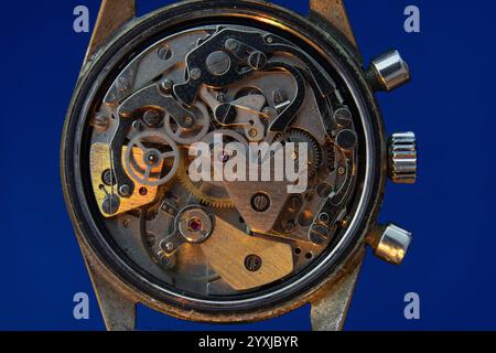 Vecchio meccanismo orologio con luce incidente gialla e sfondo blu Foto Stock