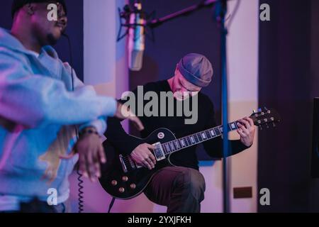 Musicisti che si esibiscono insieme in uno studio di registrazione con chitarra e microfono Foto Stock