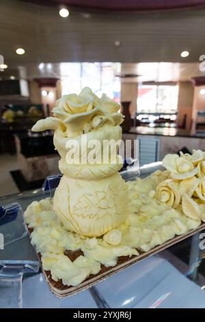 Una torta bianca con un fiore in cima viene visualizzata su un tavolo. La torta è decorata con una glassa gialla e ha una base bianca. La torta è posta su un Foto Stock