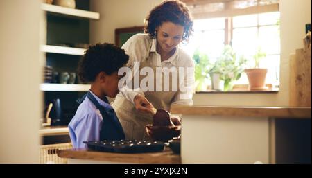 Cuocere, insegnare e bambino con la madre in cucina per sviluppare le proprie abilità con i cupcake al cioccolato. Imparare, incollare e cucinare i biscotti per bambini Foto Stock