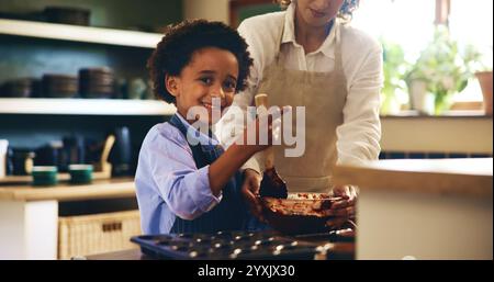 Cuocere, ritrarre e bambini con la madre in cucina per sviluppare le proprie abilità con i cupcake al cioccolato. Insegnare, legare e cucinare biscotti per bambini Foto Stock