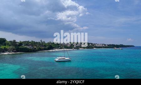 Una splendida vista costiera caratterizzata da uno yacht bianco ancorato su acque turchesi cristalline vicino a un lussuoso resort con ville a forma di piramide. Le lu Foto Stock