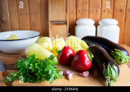 Una varietà di verdure fresche, tra cui melanzane, peperoni e aglio, sono disposte ad arte su un tagliere di legno, pronto per la preparazione Foto Stock