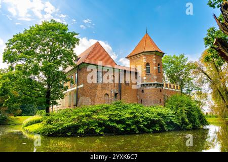 Oporow, Polonia - 17 agosto 2024: Cavalieri medievali in mattoni gotici castello di Oporowskich con fossato bagnato e ponte levatoio all'interno del parco storico nel villaggio di Oporow Foto Stock