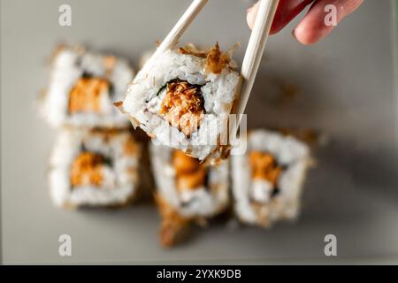 Bacchette che prendono una porzione di sushi roll. Panini di sushi con formaggio cremoso di salmone e cetriolo. Isolato. Sushi roll su sfondo grigio. Foto Stock
