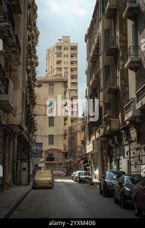 Una strada stretta e suggestiva ad Alessandria, in Egitto, che presenta antichi edifici storici con balconi, moderni e alti appartamenti e auto parcheggiate. Foto Stock