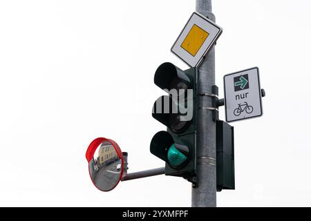 Un semaforo verde, con un cartello per la bicicletta che indica una pista ciclabile. Uno specchio riflette l'ambiente circostante, suggerendo un'area urbana trafficata. Foto Stock