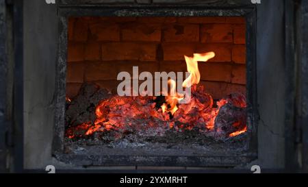 Legna e ceneri bruciate con fiamma all'interno di un vecchio forno in mattoni in formato widescreen Foto Stock