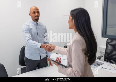 Candidato afroamericano eccitato che entra nell'ufficio riunioni, stringendo la mano con una manager indiana. Concetto di reclutamento. Foto Stock