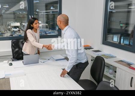Un uomo afroamericano sorridente che entra nell'ufficio aziendale e incontra HR, una bella giovane donna indiana, per un colloquio di lavoro. Foto Stock