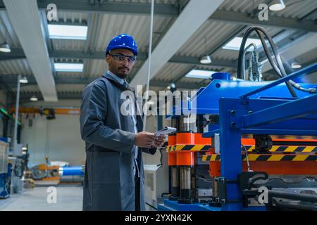 Ingegnere afroamericano addetto alla manutenzione in uno stabilimento industriale, esaminando attentamente la lista di controllo e i macchinari con una torcia, primo piano. Foto Stock