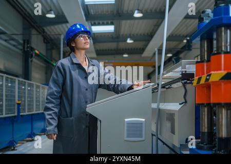 Ingegnere donna indiana con casco blu e occhiali di sicurezza, funzionamento di un pannello di controllo, controllo e automazione dei processi industriali. Foto Stock
