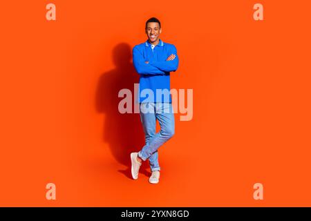 Giovane sorridente in una camicia blu vivace che posa su uno sfondo arancione brillante Foto Stock