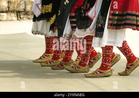 Folklore bulgaro. Le ragazze ballano folk. Le persone in costumi tradizionali ballano le danze popolari bulgare. Primo piano delle gambe femminili con sho tradizionale Foto Stock