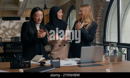 Tre donne d'affari ragazze donne d'affari multirazziali donne d'affari multietniche asiatiche caucasiche musulmane colleghi di squadra felici discutere documenti Foto Stock