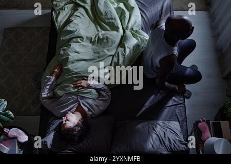 Colpo dall'alto di coppia birazziale a letto, uomo che soffre di insonnia mentre la sua amata moglie dorme tranquillamente Foto Stock