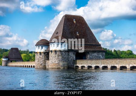 Un grande edificio in pietra con un campanile siede su un lago. L'edificio e' circondato da alberi e l'acqua e' calma. La scena ha una serena e pacifica Foto Stock