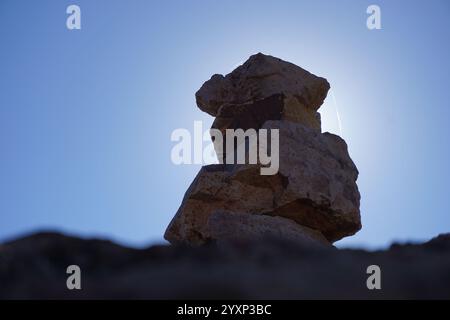 Una grande pila di rocce con un sole luminoso che splende sopra di essa. Il sole è posizionato al centro delle rocce, creando un contrasto sorprendente tra il buio Foto Stock