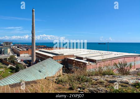 Savona, Italia - 17 dicembre 2024: Complesso industriale in riva al mare, con alti fumogeni, grandi edifici e navi lontane, che illustrano i juxtapos Foto Stock