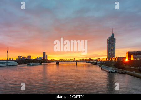 Alba ardente sul Danubio Donau, nave da crociera, ponte Nordbahnbrücke, grattacieli a Donaucity con Torre DC 1, Millennium Tower a destra Vienna 20. BR Foto Stock