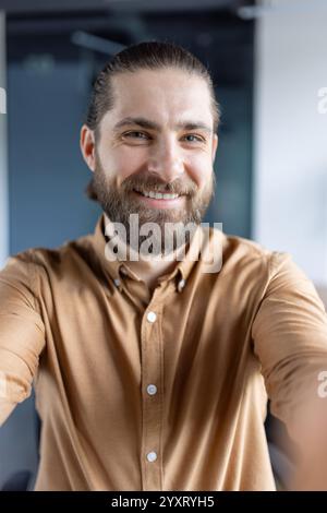 Una persona allegra in un abbigliamento casual che cattura un selfie in ufficio, sottolineando la professionalità cordiale e disponibile. Foto Stock