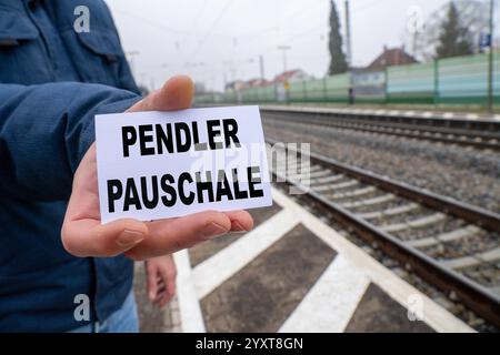 Baviera, Germania - 17 dicembre 2024: Una persona ha un cartello con il testo PENDLERPAUSCHALE. Immagine simbolica per sgravi fiscali, costi di mobilità e spostamenti. FOTOMONTAGGIO *** Eine person hält ein Schild mit dem Text PENDLERPAUSCHALE. Symbolbild für steuerliche Entlastungen, Mobilitätskosten und Arbeitswege. FOTOMONTAGE Foto Stock