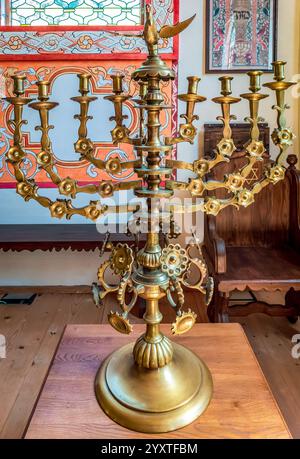 Sanok, Polonia - 4 maggio 2024. Vista ravvicinata di una menorah in ottone splendidamente realizzata, in piedi su un tavolo di legno in una replica di un legno del XVIII secolo Foto Stock