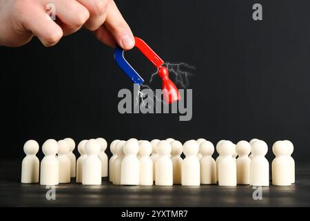 Uomo con magnete che attrae un pezzo rosso tra quelli bianchi al tavolo nero, primo piano Foto Stock