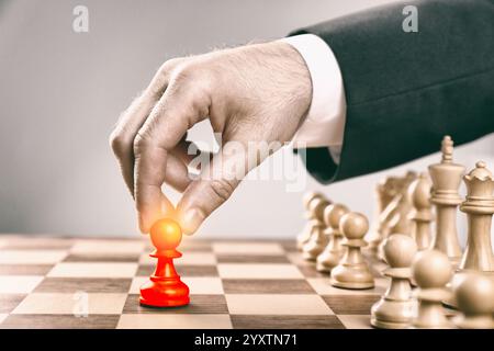 Uomo che fa la prima mossa posizionando un pedone rosso su una scacchiera di legno, primo piano Foto Stock