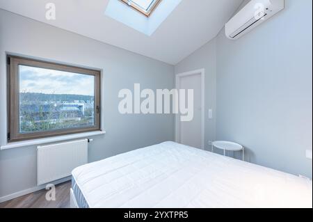 Camera da letto luminosa e pulita, dotata di un comodo letto, armadio a muro bianco, lucernario e design minimalista, atmosfera perfetta per il relax. Min. Moderna Foto Stock