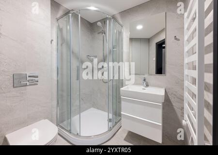 Bagno contemporaneo con box doccia in vetro, elegante lavabo bianco, pareti piastrellate grigie e servizi moderni in un ambiente pulito e minimalista Foto Stock