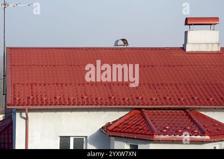 Pendenza del tetto coperta da lamiere di metallo effetto piastrella di colore rosso brillante. Foto Stock