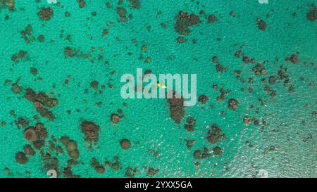 Vista aerea di un kayak che pagaia su un kayak giallo in acque tropicali turchesi poco profonde tra le barriere coralline, creando un incredibile contrasto di colori Foto Stock