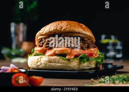 Gustoso hamburger di tonno alla griglia o panino con lattuga, pomodoro, cipolla e maionese serviti su un tavolo di legno. umore oscuro. Foto Stock