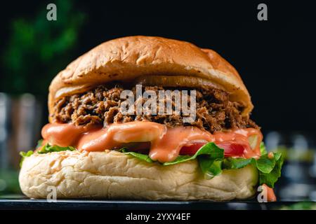 Gustoso hamburger di tonno alla griglia o panino con lattuga, pomodoro, cipolla e maionese serviti su un tavolo di legno. umore oscuro. Foto Stock