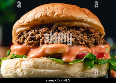 Gustoso hamburger di tonno alla griglia o panino con lattuga, pomodoro, cipolla e maionese serviti su un tavolo di legno. umore oscuro. Foto Stock