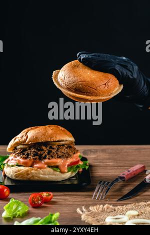 Gustoso hamburger di tonno alla griglia o panino con lattuga, pomodoro, cipolla e maionese serviti su un tavolo di legno. umore oscuro. Foto Stock