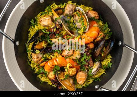 Vista dall'alto della tradizionale paella di pesce spagnola con riso, cozze e gamberi in una padella su un tavolo di legno Foto Stock