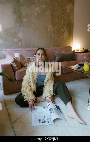 Ritratto di una giovane donna seduta sul pavimento con una rivista vicino al divano di casa Foto Stock