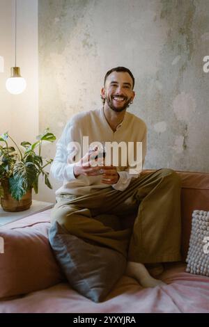 Ritratto di un uomo felice che tiene in mano wineglass mentre si siede sul divano a casa Foto Stock