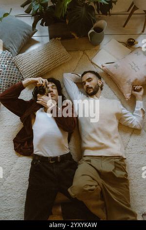 Ritratto ad angolo alto di un uomo sdraiato accanto al fidanzato che tiene la fotocamera a casa Foto Stock