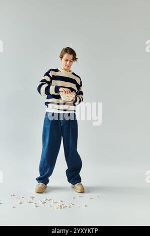 Un giovane studente elegante si trova in uno studio, maneggiando giocosamente popcorn mentre è vestito con calore. Foto Stock