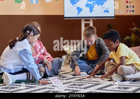 Ripresa completa di diversi gruppi di bambini che imparano l'inglese seduto sul pavimento in classe e giocano insieme a una partita di corrispondenza lettere Foto Stock