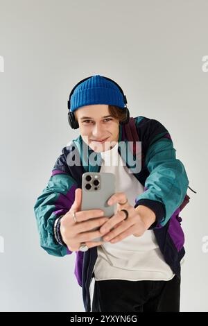 Un giovane uomo con un bomber alla moda sorride mentre scatta un selfie in uno studio. Foto Stock