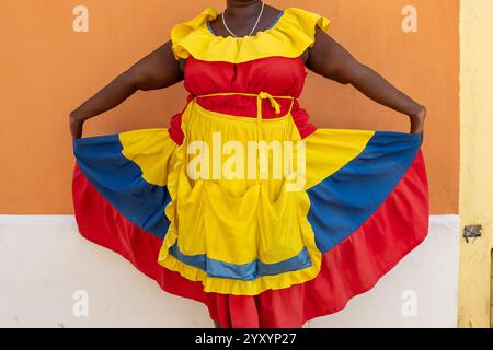 Primo piano del colorato abito tradizionale di Una donna Palenquera in giallo, rosso e blu con le mani tese Foto Stock
