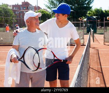 Nonno e nipote che parlano sul campo a giocare a tennis Foto Stock