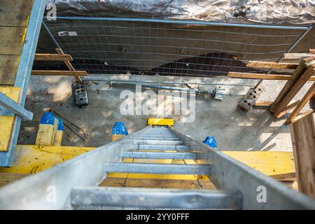 Vista dall'alto di una lunga scala in alluminio argento appoggiata contro la parete della casa. Vista ravvicinata dalla parte superiore della scaletta a gradini sul tetto. lavorare in altezza. L Foto Stock