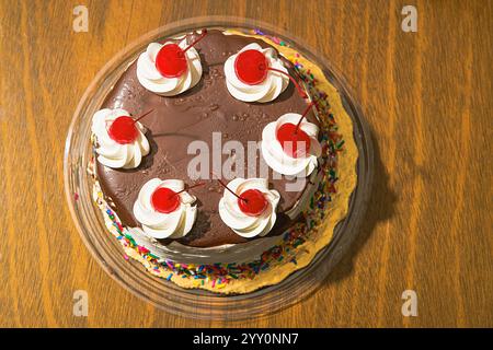 Una decadente torta al cioccolato condita con ciliegie lucide, un turbinio di panna montata e una spruzzata di coriandoli colorati. Foto Stock